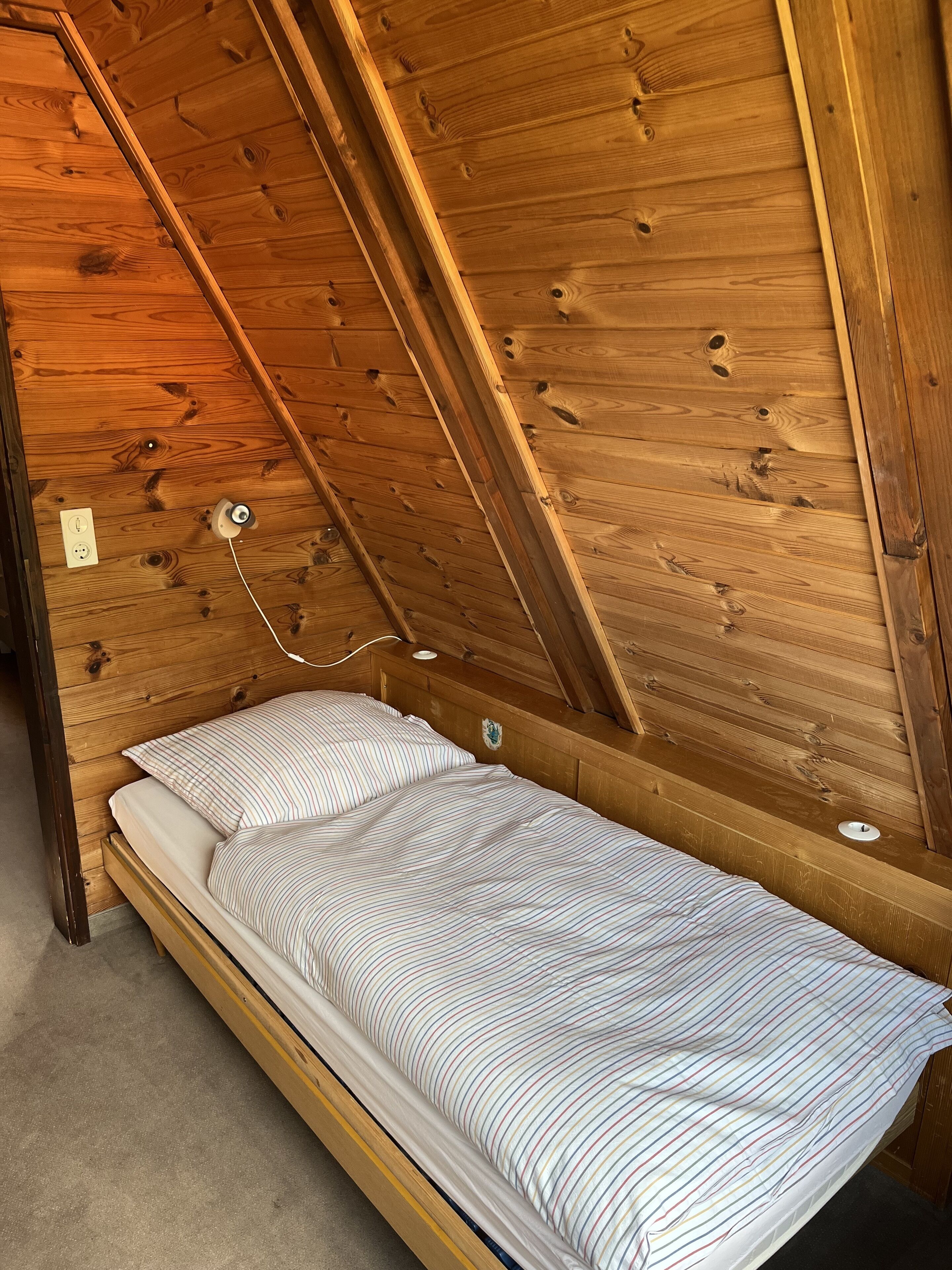 Una habitación pequeña con cama individual, techo inclinado y paredes de madera.