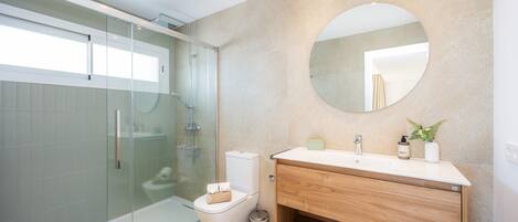 A modern bathroom with a glass shower enclosure, a toilet, a sink with a mirror, and a trash can.