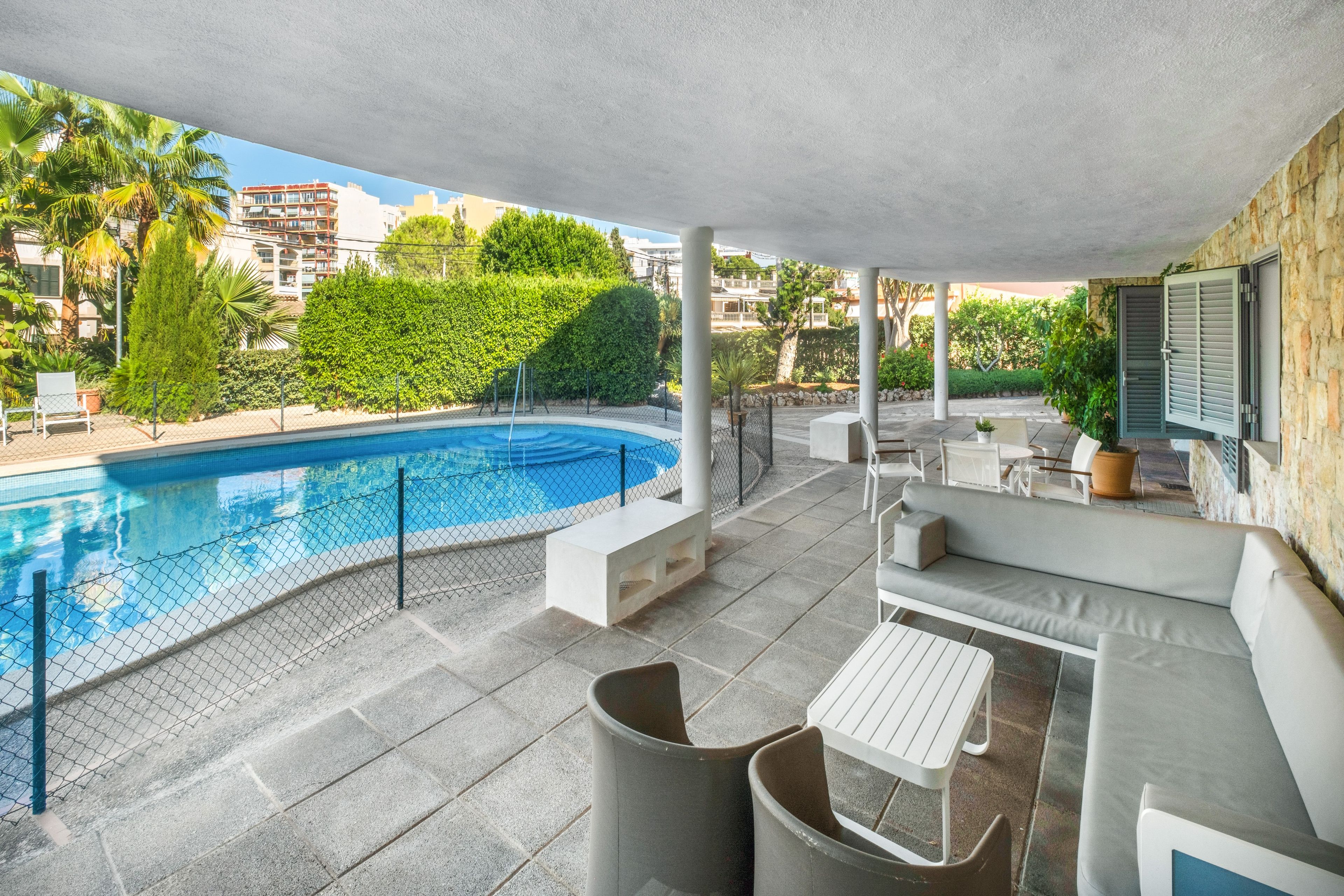 A covered outdoor swimming pool area with a curved pool, seating, and a view of the surrounding buildings and greenery.