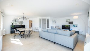 Un salon moderne comprenant un canapé, une table à manger, des chaises, un téléviseur et un coin cuisine.