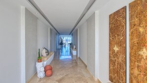Un pasillo con suelo de mármol, paredes blancas y un panel decorativo a la derecha.
