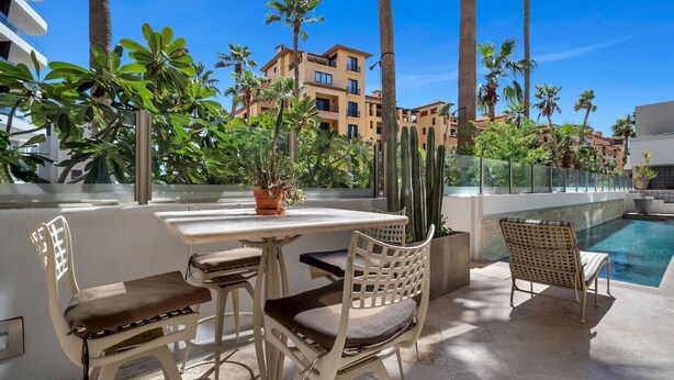Un patio al aire libre con mesa y sillas, una piscina y palmeras.