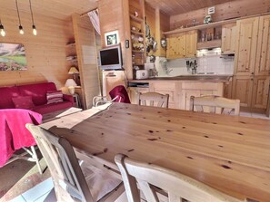 Ein gemütliches Blockhaus-Interieur mit einem Holzespeisetisch, Stühlen, einem roten Sofa und einer Küchenzeile mit Holzschränken und einer weißen Arbeitsplatte.