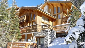 Una cabaña de madera con cimientos de piedra, balcones de madera y un paisaje cubierto de nieve.