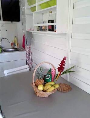 A kitchen with white cabinets, a sink, and a countertop. There is a basket with fruits and a wooden spoon on the counter. - GITE DE CHARME fleuri à Petit Bourg : Self-catering accommodation (PETIT-BOURG)