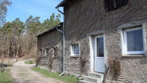 A rustic stone building with a dirt path leading to the entrance, surrounded by trees. - Vacation apartment on the Amazon of the North - Holiday apartment (Demmin)