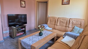 A living room with a sofa, a television, a coffee table, and a door. - Vacation apartment on the Amazon of the North - Holiday apartment (Demmin)