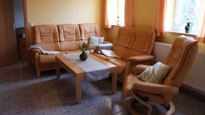 A living room with a sofa set, a coffee table, and a rocking chair. There is a window with curtains, a radiator, and a picture on the wall. - Vacation apartment on the Amazon of the North - Holiday apartment (Demmin)