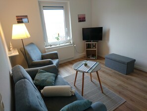 En stue med sofa, lænestol, fjernsyn og et lille bord med en plante.