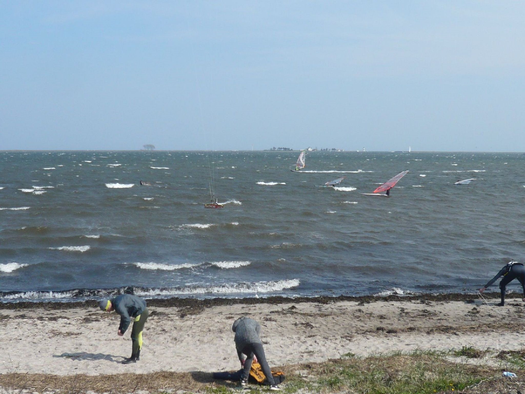 Ein Strand mit Menschen am Ufer und Segelbooten im Wasser.