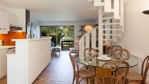 Une cuisine moderne avec une table et des chaises en verre, un escalier en colimaçon et une vue sur un jardin et un espace de détente extérieur.