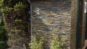 A stone building with a metal roof, a star-shaped outdoor floor design, and a small garden area with plants and a pink flamingo statue. - The colonial furnished short-term (Saint-Malo)