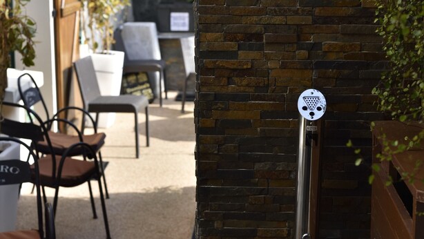 An outdoor seating area with chairs and tables, a stone wall with a metal sign, and a door with a sign indicating a public restroom. - The colonial furnished short-term (Saint-Malo)