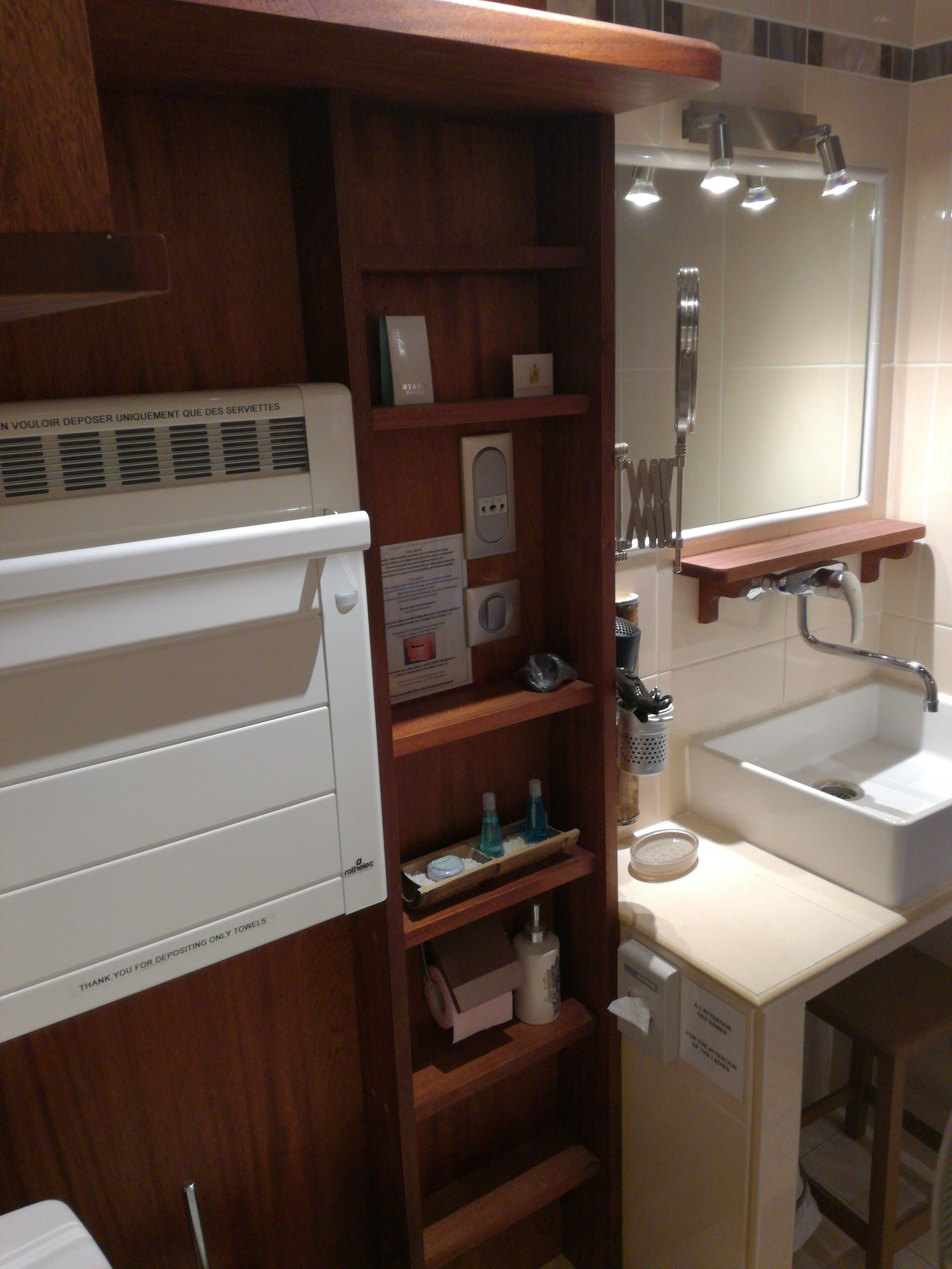 A bathroom with a white sink, wooden shelves, a mirror, and a towel dispenser.