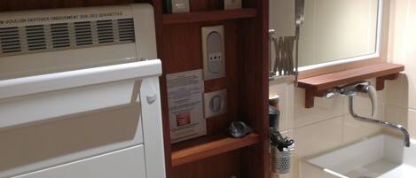 A bathroom with a white sink, wooden shelves, a mirror, and a towel dispenser.