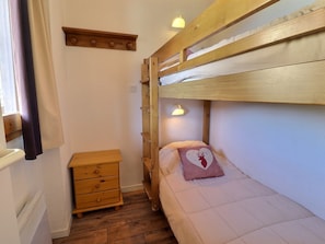 A compact room with a bunk bed, a bedside table, a lamp, and a window with curtains.