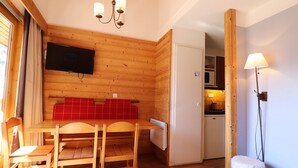 A wooden interior with a dining table and chairs, a television mounted on the wall, and a kitchen area visible through an open door. - Charming 2-Story Duplex, Ski-In, Perfect for Families (Méribel)