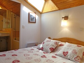 A bedroom with a wooden ceiling, a bed with patterned bedding, a bedside lamp, and a framed picture on the wall.