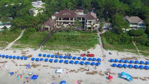 An aerial view of a beach with numerous blue umbrellas and a large house with a driveway leading to it. - 10 Night Heron | 1 Bedroom Villa | On-site Pool | Walk to Beach | STR #027222 (Hilton Head Island)