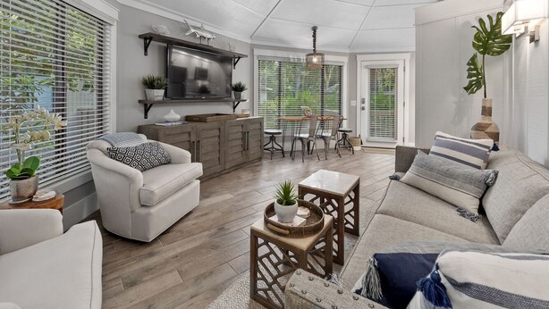 A spacious living area with a sofa, armchairs, a dining table, and a kitchen area with a TV and cabinets. - 10 Night Heron | 1 Bedroom Villa | On-site Pool | Walk to Beach | STR #027222 (Hilton Head Island)