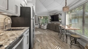 A modern kitchen with a marble countertop, stainless steel appliances, and a dining area with a wooden table and chairs. - 10 Night Heron | 1 Bedroom Villa | On-site Pool | Walk to Beach | STR #027222 (Hilton Head Island)