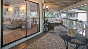 A covered patio area with a sliding glass door leading to a living room, furnished with a sofa, chairs, and a table. - 10 Night Heron | 1 Bedroom Villa | On-site Pool | Walk to Beach | STR #027222 (Hilton Head Island)