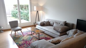 A living room with a grey sofa, a matching armchair, a coffee table, a floor lamp, and a colorful rug. - Large and Charming Apartment in Obernai (Obernai)