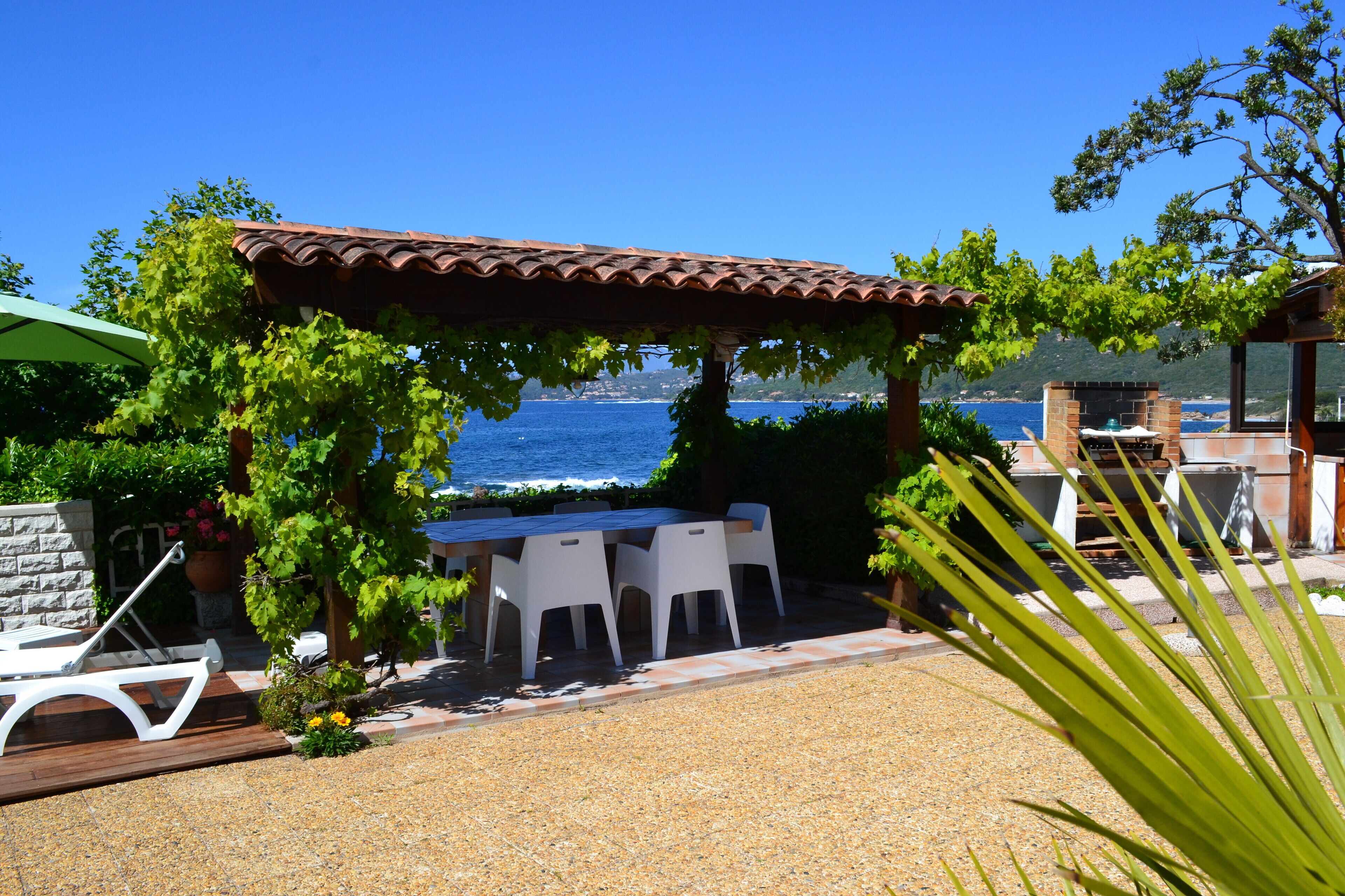 Um pátio com pérgola, cadeiras brancas e uma mesa com vista para o mar.