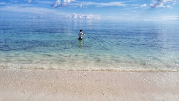 Une plage avec une eau claire et une personne qui pêche.