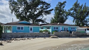 Une propriété située en bord de mer, comprenant deux maisons aux couleurs turquoise, une plage de sable et une vue dégagée sur l’océan.