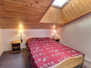 A bedroom with a sloped ceiling, wooden walls, a bed with a red blanket, two bedside tables with lamps, and a skylight.