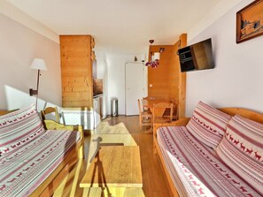 A cozy room with a wooden floor, a bed with patterned bedding, a small wooden table, and a TV mounted on the wall.