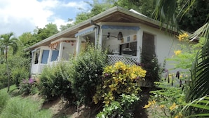 A single-story house with a porch, surrounded by lush greenery and flowering plants.