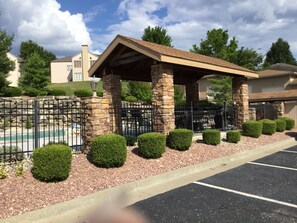 Enjoy the serene surroundings of this property with a paved parking area, neatly trimmed bushes, and a secure stone and metal fence.