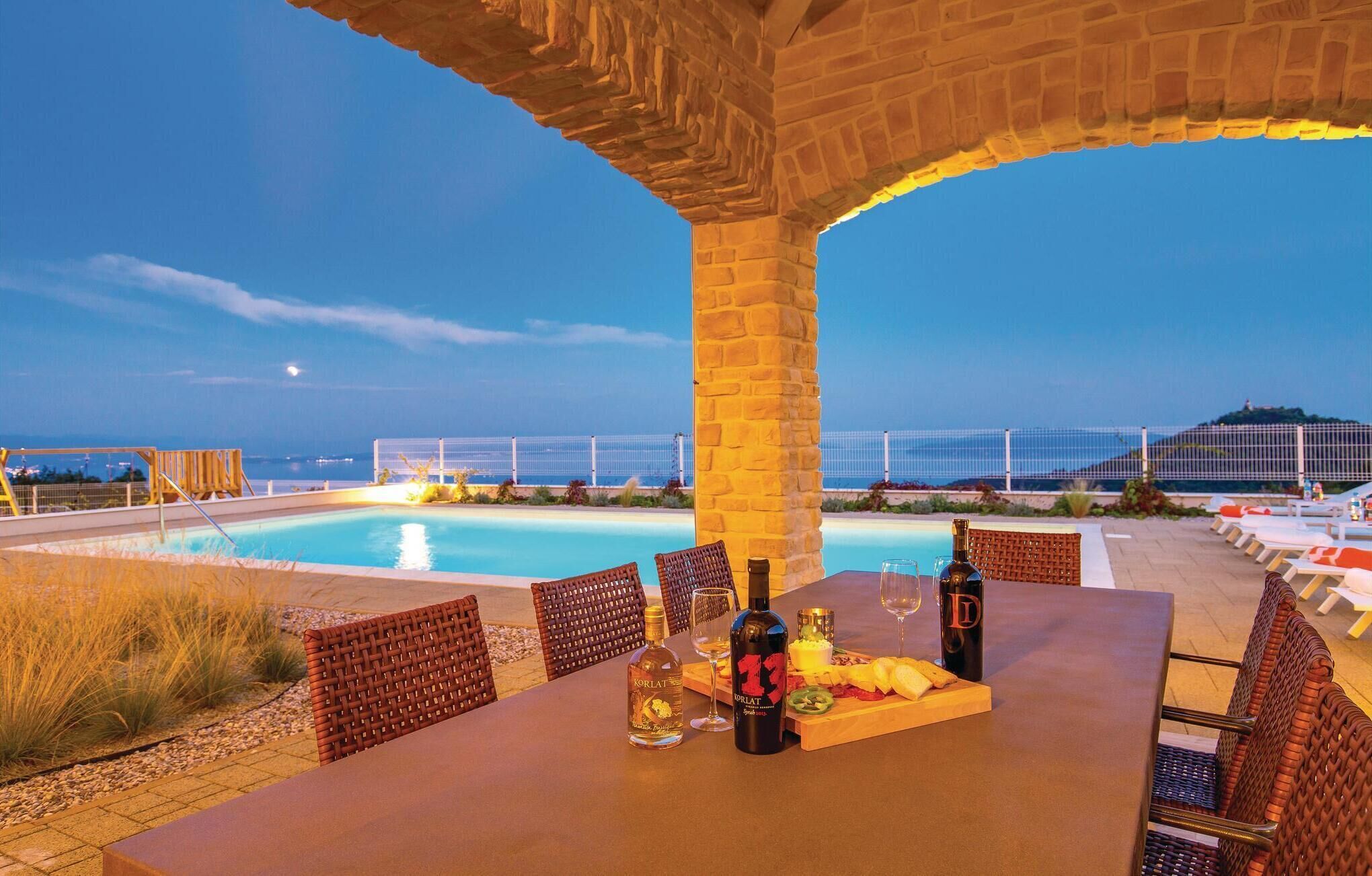 Área de piscina externa com mesa posta para refeições, rodeada por cadeiras de vime.