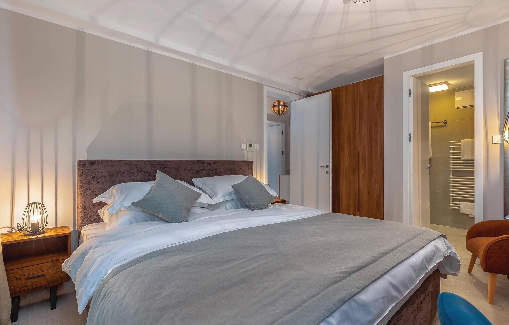 Een moderne slaapkamer met een groot bed, een houten garderobe, een blauwe stoel en een douchecabine met glazen wanden.