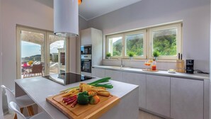 A modern kitchen with a central island, a built-in oven, and a window overlooking greenery. - Gorgeous home in Veprinac with sauna (Veprinac)