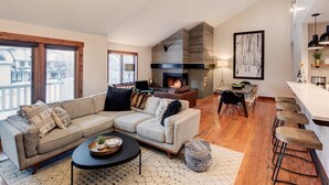 A modern living room with a sectional sofa, a fireplace, and a dining area with bar stools.