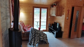 Ein gemütliches Blockhaus-Interieur mit Kamin, einer Couch mit Zebra-Decke, einem Fernseher und Holzwänden.