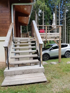 Eine Holztreppe führt zu einem Deck, in der Nähe steht ein Auto.