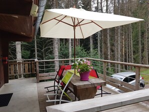 Eine Holzterrasse mit Tisch, Stühlen, einem großen Sonnenschirm und einem Blumentopf.