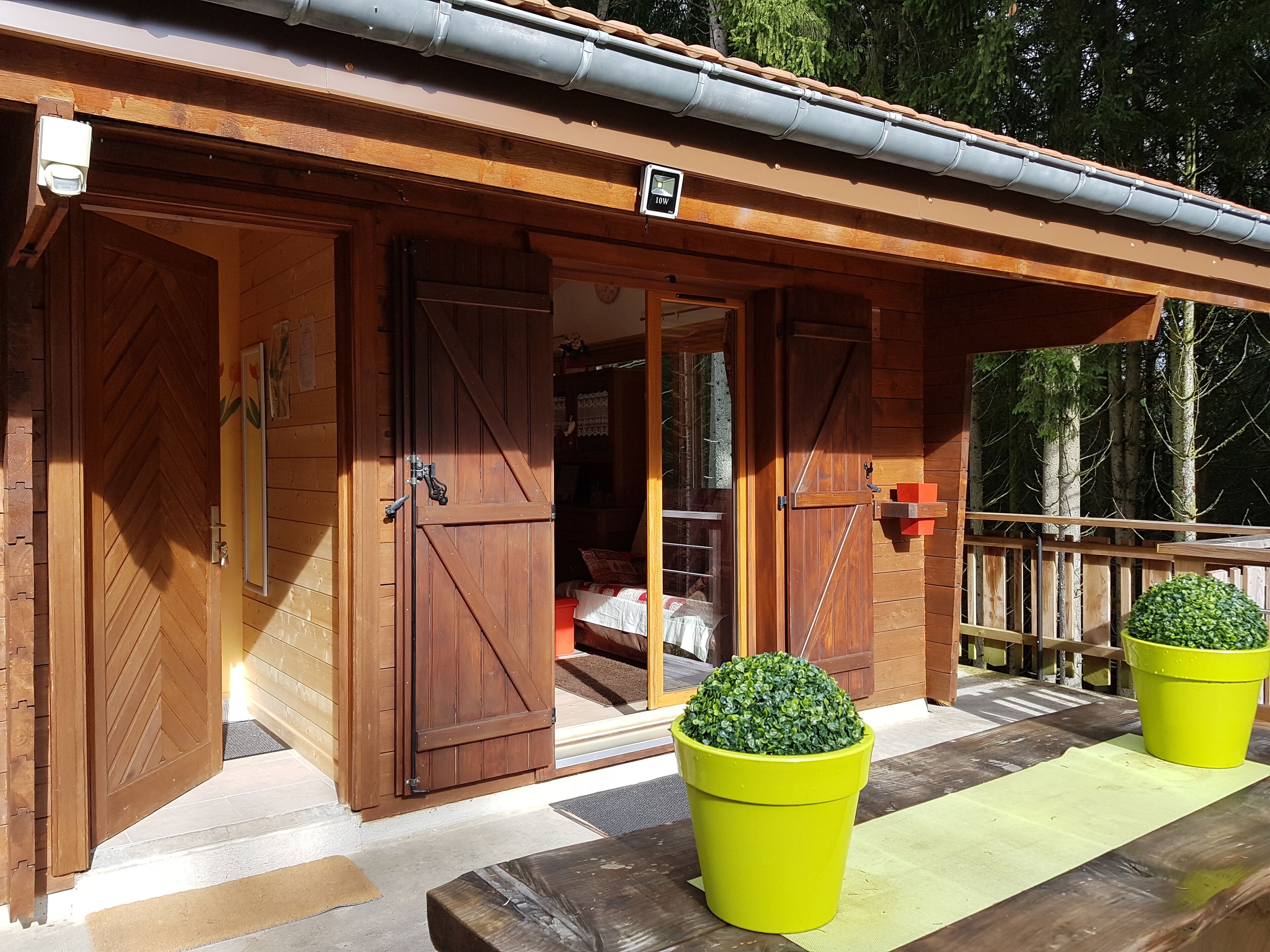 A wooden cabin with large sliding doors, a covered porch, and two potted plants.