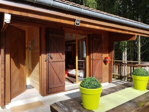 A wooden cabin with large sliding doors, a covered porch, and two potted plants.