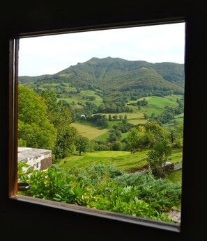 Vista de un valle verde con colinas y una montaña distante a través de una ventana.
