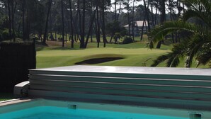 Ein Swimmingpool mit Blick auf einen Golfplatz und Bäume im Hintergrund.