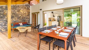 A dining area with a wooden table set for six, surrounded by black chairs, and a stone wall in the background. - Escale Chic!  Charming villa in Saint-Gilles-Les-Bains (Saint-Gilles les Bains)