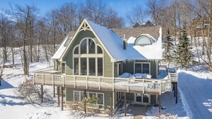 Ein großes, zweistöckiges Haus mit breitem Veranda und überdachter Terrasse, umgeben von Schnee und Bäumen.