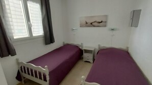 A small, clean room with two single beds, a small table, and a window with curtains.