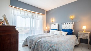 A bedroom with a large bed, two bedside tables with lamps, a wooden dresser, and a window with sheer curtains. - Duplex Apartment 65m2 in quiet residence in Uzès, free Parking, garage in Option (Uzès)
