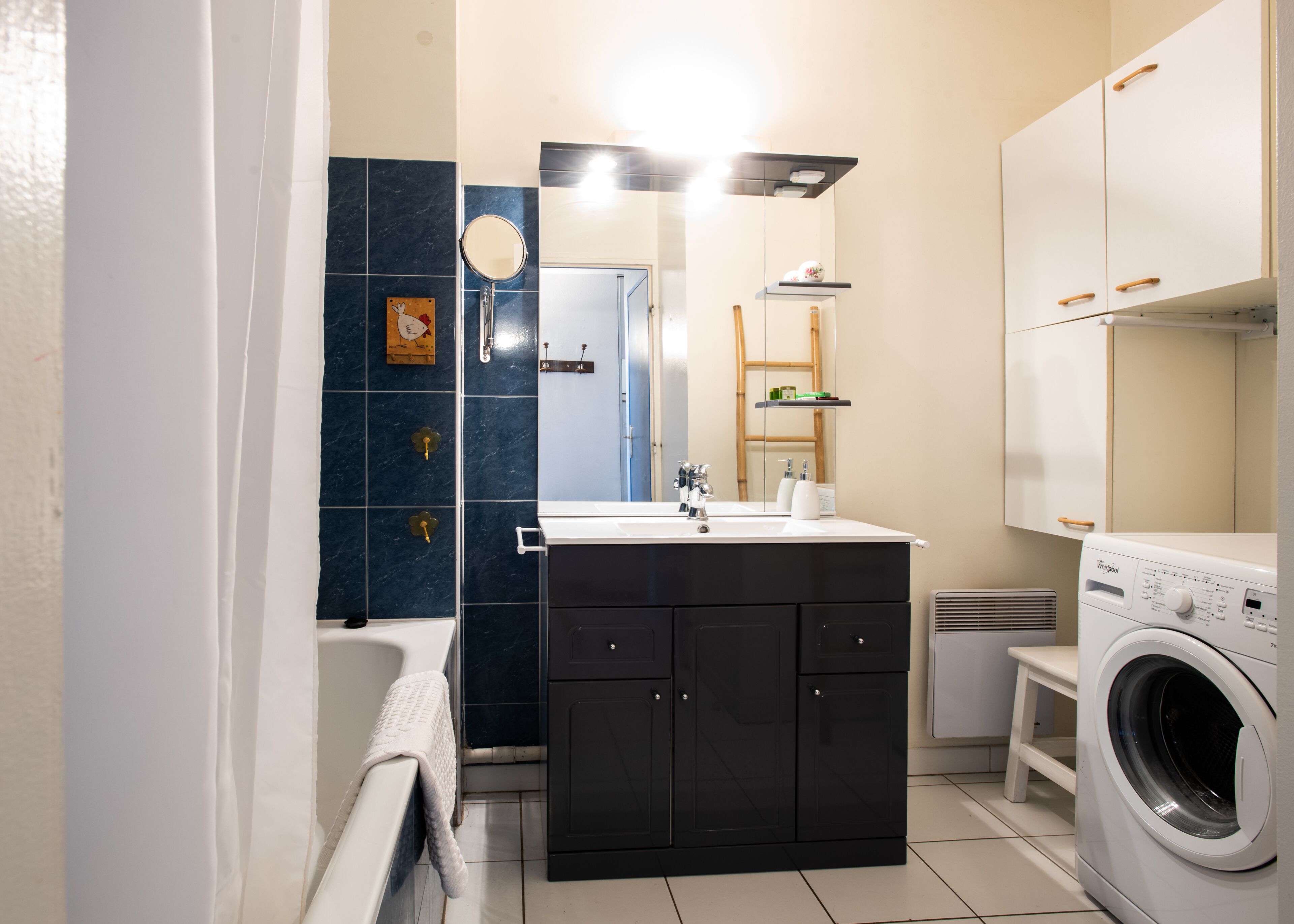 A modern bathroom with a black vanity, a white sink, a mirror, a toilet, a shower, and a washing machine.